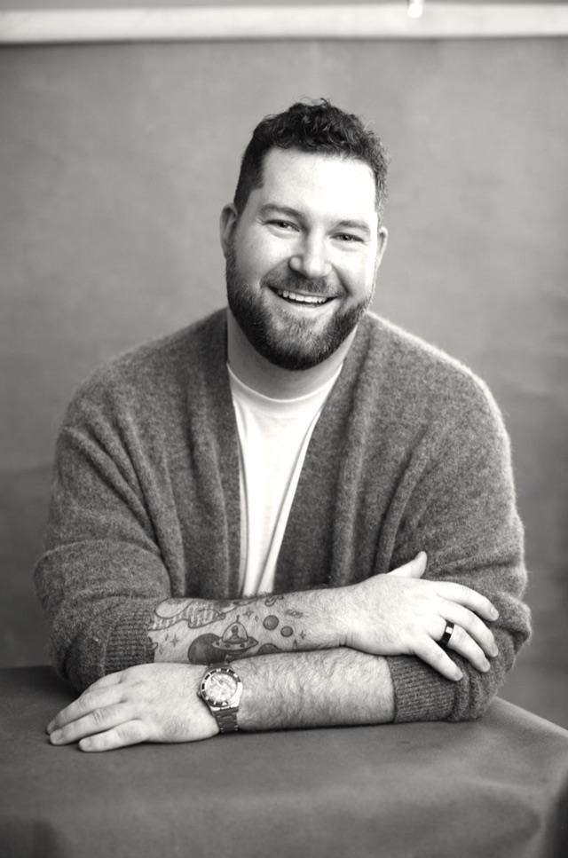 Black-and-white portrait of Martin Laws, smiling with his arms crossed on a table